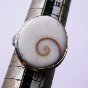Könnte beinhalten: Ein silberner Ring mit einem weißen ovalen Muschelkamee mit einem braunen Spiralmuster.