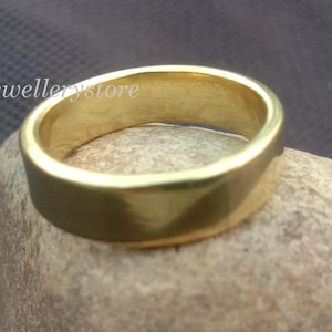 Könnte beinhalten: Ein goldfarbener Ring mit flachem Band, der auf einem hellbraunen Stein liegt. Der Ring hat eine glatte, polierte Oberfläche und ein schlichtes Design. Der Ring ist ein Schmuckstück, wahrscheinlich für den täglichen Gebrauch.