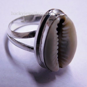 Könnte beinhalten: Ein silberner Ring mit einer weißen Kaurischnecke in der Mitte. Der Ring hat ein Doppelband-Design.