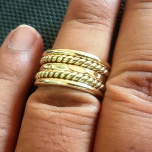 Puede incluir: Un anillo dorado con un diseño de cuerda trenzada. El anillo, que se lleva en un dedo, tiene múltiples bandas con el patrón de cuerda. Una joya llamativa.