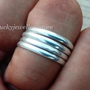 Könnte beinhalten: Nahaufnahme einer Hand mit vier silbernen Ringen, die übereinander getragen werden. Die Ringe sind glatt und haben ein minimalistisches Design. Im Hintergrund ist der Text "luckyjewellerystore" zu sehen.