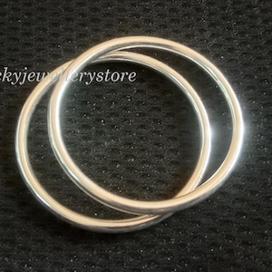 Könnte beinhalten: Zwei silberne Ringe, die sich verschlingen und eine Acht bilden. Die Ringe sind glatt und reflektierend, vor einem dunklen, strukturierten Hintergrund. Der Text "Luckyjewelrystore" ist oben links sichtbar.