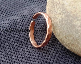 Op de afbeelding: Een koperkleurige ring met een open ontwerp en een gehamerd, getextureerd oppervlak. De band heeft een licht onregelmatige, organische vorm met een metallic afwerking en vertoont een duidelijke roodbruine tint in het metaal.