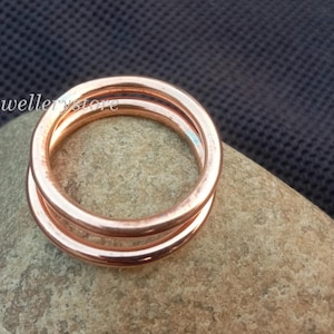 Könnte beinhalten: Ein Stapel von drei kupferfarbenen Ringen liegt auf einem hellbraunen Stein vor einem dunkelblauen, strukturierten Hintergrund. Die Ringe sind kreisförmig und scheinen aus Metall zu sein. Die Ringe sind übereinander gestapelt.