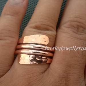 Könnte beinhalten: Ein kupferfarbener Ring mit gehämmertem Muster. Der Ring wickelt sich mit einem Spiraldesign um den Finger. Der Ring besteht aus Metall und hat ein glänzendes Finish. Der Ring ist ein Schmuckstück.