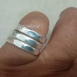 Könnte beinhalten: Drei silberne Ringe mit gehämmerten Strukturen sind auf einem Finger gestapelt. Die Ringe haben eine glänzende, reflektierende Oberfläche. Die Ringe sind ein schlichtes, elegantes Design. Die Ringe sind eine Art Schmuck.