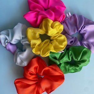 Puede incluir: Cinco scrunchies coloridos en una variedad de colores, incluyendo amarillo, verde, rojo, morado y rosa. Los scrunchies están hechos de una tela suave y sedosa y son perfectos para sujetar el cabello en su lugar.