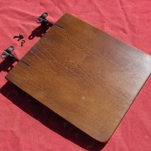 May include: A brown wooden shelf with two black metal hinges attached to the top. The shelf is on a red fabric surface.