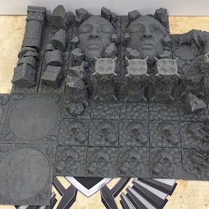 May include: A set of gray 3D printed dungeon tiles for tabletop gaming. The tiles feature a variety of textures and designs, including skulls, faces, and columns. There are also several smaller pieces, such as walls and debris.