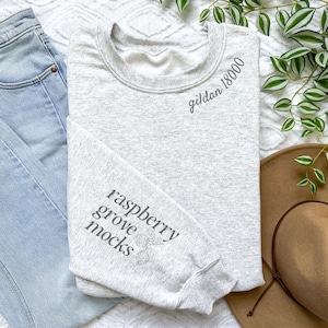 May include: A gray sweatshirt with the text "gildan 18000" on the front and "raspberry grove mocks" on the sleeve.