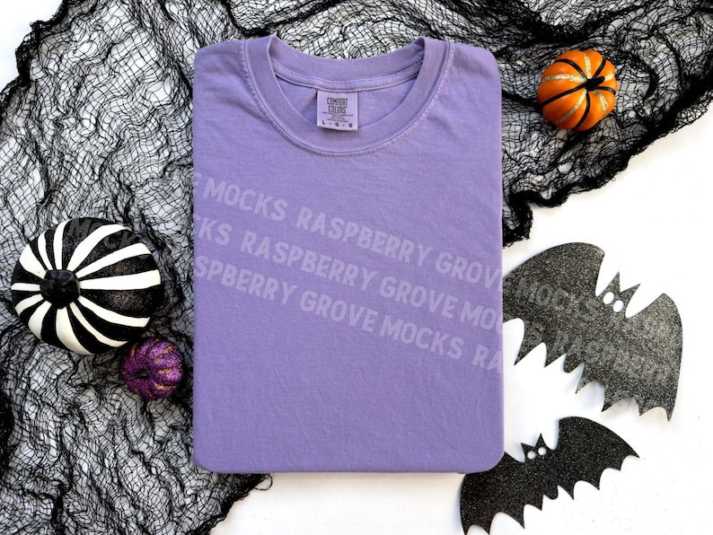 May include: A purple t-shirt with the text "Raspberry Grove" repeated on the front. The t-shirt is laying on a black mesh fabric with black bats and pumpkins.