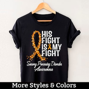 May include: Black t-shirt with an orange ribbon made of hearts and the text "His Fight Is My Fight" and "Sensory Processing Disorder Awareness".