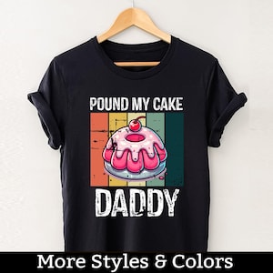 Puede incluir: Camiseta negra con un gráfico vintage de un pastel con el texto "Pound My Cake Daddy".
