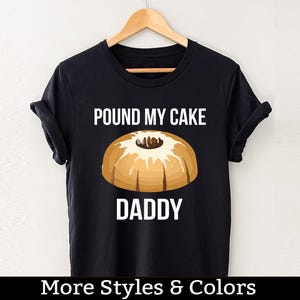 Puede incluir: Camiseta negra con texto blanco que dice "Pound My Cake Daddy" y un gráfico de un pastel de libra.
