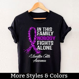 May include: Black t-shirt with a purple ribbon made of hearts and the text "In this family nobody fights alone" and "Ulcerative Colitis Awareness".