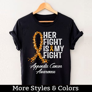 Puede incluir: Camiseta negra con una cinta naranja hecha de corazones y el texto "Her Fight Is My Fight" y "Appendix Cancer Awareness".
