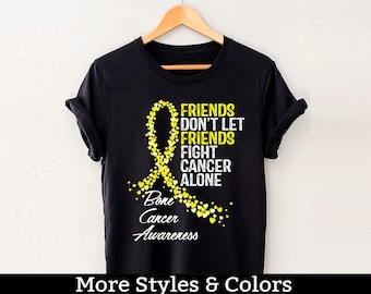 May include: Black t-shirt with a yellow ribbon made of hearts and the text "Friends Don't Let Friends Fight Cancer Alone" and "Bone Cancer Awareness".