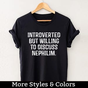 Könnte beinhalten: Schwarzes T-Shirt mit weißem Text, der "Introvertiert, aber bereit, über Nephilim zu diskutieren" lautet.