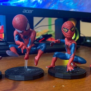 Peut inclure: Quatre figurines de Spider-Man rouges et bleues avec des yeux noirs et des accents blancs. Chaque figurine est pos&eacute;e dans une pose d'action diff&eacute;rente et se tient sur une base noire.
