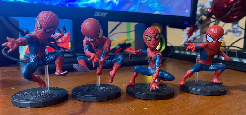 Peut inclure: Quatre figurines de Spider-Man rouges et bleues avec des yeux noirs et des accents blancs. Chaque figurine est pos&eacute;e dans une pose d'action diff&eacute;rente et se tient sur une base noire.