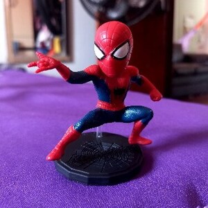 Peut inclure: Une figurine d'action Spider-Man rouge et bleue avec une base en forme de toile d'araign&eacute;e. La figurine est pos&eacute;e dans une position d'action dynamique, une jambe lev&eacute;e.
