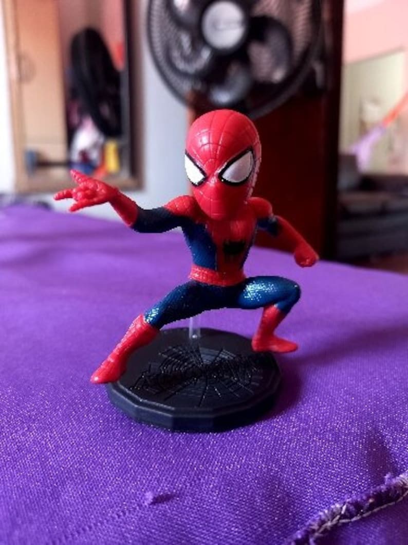 Peut inclure: Une figurine d'action Spider-Man rouge et bleue avec une base en forme de toile d'araign&eacute;e. La figurine est pos&eacute;e dans une position d'action dynamique, une jambe lev&eacute;e.