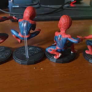Peut inclure: Quatre figurines d'action Spider-Man rouges et bleues sur des socles noirs avec des supports en plastique transparent. Les figurines sont pos&eacute;es dans diff&eacute;rentes poses d'action.
