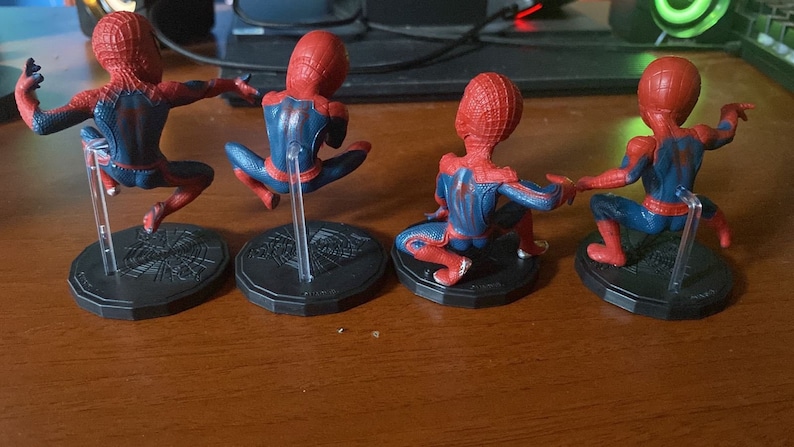 Peut inclure: Quatre figurines d'action Spider-Man rouges et bleues sur des socles noirs avec des supports en plastique transparent. Les figurines sont pos&eacute;es dans diff&eacute;rentes poses d'action.