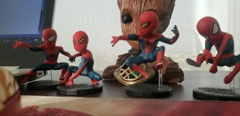 Peut inclure: Quatre figurines de Spider-Man rouges et bleues, chacune dans une pose diff&eacute;rente. Les figurines sont pos&eacute;es sur des socles noirs avec un logo Spider-Man blanc.