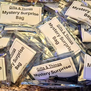 May include: A pile of clear plastic bags, each labelled "Gifts & Things Mystery Surprise Bag." The bags contain a vintage keyring. The bags are arranged on a woven surface, creating a textured background.