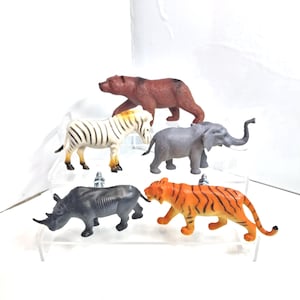 May include: A selection of plastic toy animals, including a brown bear, a zebra with black and white stripes, a grey elephant, a grey rhinoceros, and an orange tiger with black stripes. The toys are displayed on clear, tiered shelves.