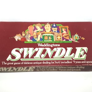 May include: A vintage "Swindle" board game box by Waddingtons. The maroon box displays the game title in large white letters and a colourful illustration of characters. The text reads "The great game of dubious antique dealing for 3 to 6 'swindlers' 9 years and upwards."