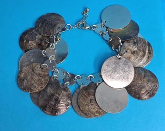 May include: A charm bracelet featuring alternating circular discs. The bracelet consists of polished silver-tone metal discs and textured, dark brown, circular shell-like discs connected by silver-tone metal jump rings and a lobster claw clasp.