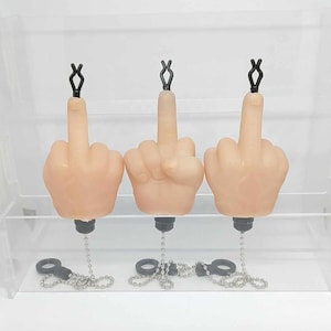May include: Three small, light-skinned, plastic hands with black chains attached to the wrists. Each hand is making the middle finger gesture.
