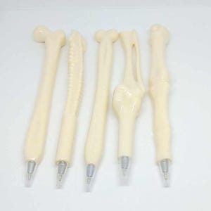 May include: Set of five bone-shaped pens with white plastic bodies and silver tips. The pens are arranged in a row on a white surface.