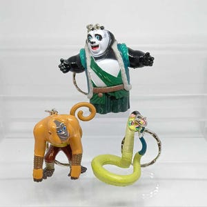 May include: Three Kung Fu Panda character keychains: a black and white panda, a brown monkey, and a green snake.