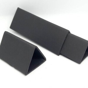 May include: Two black triangular display stands made of cardboard. The larger stand is folded to create a long, rectangular shape.