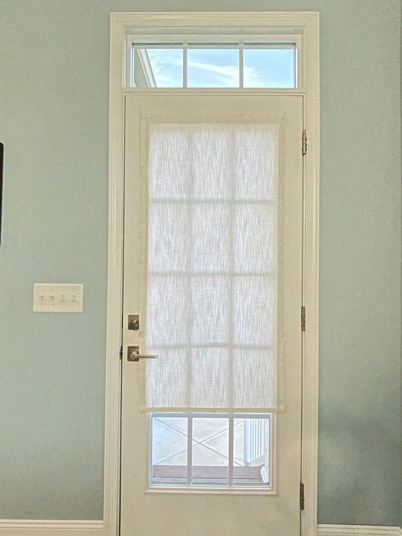 Puede incluir: Una puerta blanca con una ventana rectangular y una ventana rectangular m&aacute;s peque&ntilde;a encima. Una cortina blanca, texturizada y semitransparente cubre la ventana principal. La puerta est&aacute; colocada contra una pared azul claro, con un interruptor de luz a la izquierda.