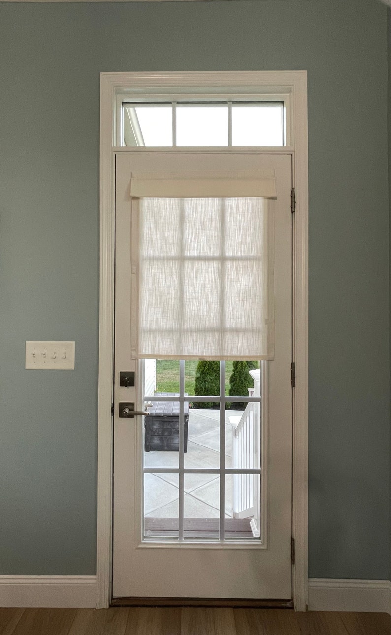 Puede incluir: Una puerta blanca con una ventana y una cortina de tela color crema. La puerta tiene un patr&oacute;n de rejilla y un tirador. La puerta est&aacute; situada en una habitaci&oacute;n con paredes azul claro y suelo de madera.