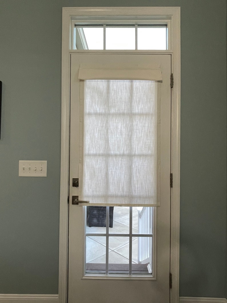 Puede incluir: Una puerta blanca con una ventana rectangular y una ventana m&aacute;s peque&ntilde;a encima. Una cortina de tela texturizada de color crema cubre la parte superior de la ventana. La puerta tiene una manija y bisagras plateadas. La pared est&aacute; pintada de azul verdoso claro.