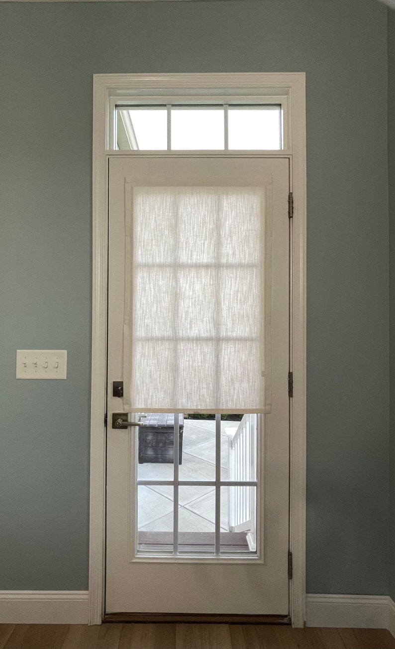Puede incluir: Una puerta blanca con un dise&ntilde;o de panel de ventana rectangular y una persiana de tela blanca. La puerta est&aacute; colocada en un marco blanco contra una pared azul claro. Una peque&ntilde;a ventana est&aacute; encima de la puerta.