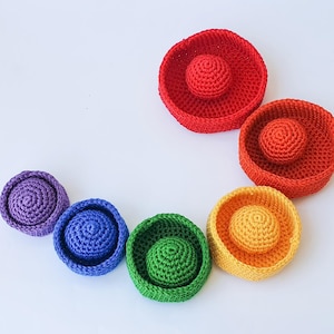 Puede incluir: Un conjunto de seis cuencos anidados de ganchillo en colores arcoíris. Los cuencos están hechos de hilo suave y son perfectos para guardar objetos pequeños.