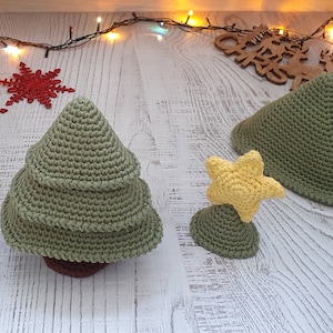 Könnte beinhalten: Zwei gehäkelte Weihnachtsbäume, einer mit einem gelben Stern oben, auf einer weißen Holzoberfläche mit einem hölzernen Weihnachtszeichen und Lichterketten.