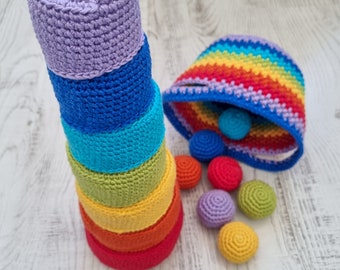 May include: A rainbow crocheted stacking toy with six colourful rings and a matching rainbow crocheted basket. The basket is filled with small crocheted balls in various colours.