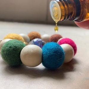 May include: A colorful felt and wooden bead bracelet with a clear crystal bead. Essential oil is being dripped onto the bracelet.
