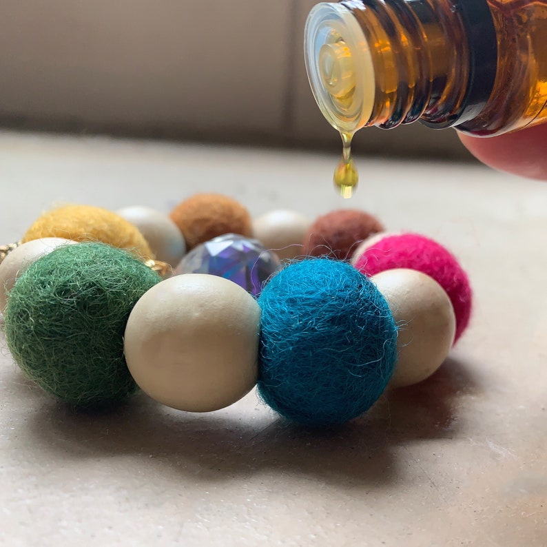 May include: A colorful felt and wooden bead bracelet with a clear crystal bead. Essential oil is being dripped onto the bracelet.