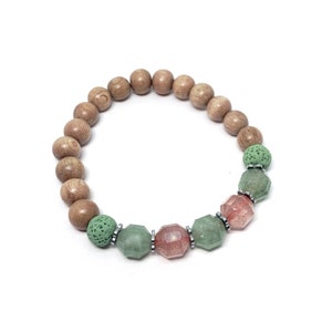 Puede incluir: Un brazalete de cuentas de madera con cuentas de piedras preciosas verdes y rosas. El brazalete es de madera natural y presenta una mezcla de cuentas redondas y facetadas.