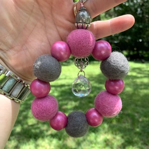 May include: A pink and gray beaded charm with a crystal pendant. The beads are made of felt and wood.