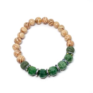 Puede incluir: Un brazalete de cuentas verdes y marrones con cuentas de madera y cuentas de piedras preciosas verdes. El brazalete tiene una cuenta de roca volcánica y cuentas espaciadoras plateadas.