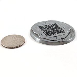 Our Channenge Coin next to a US Quarter. The coin is low-profile with 3d textures and a custom QR code stamped into the metal, with a full lifetime guarantee.